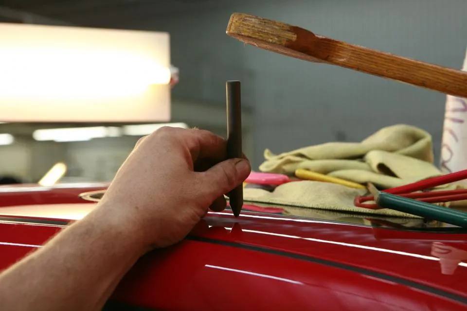 Die Hände eines Mechanikers mit Werkzeug an einem roten Auto
